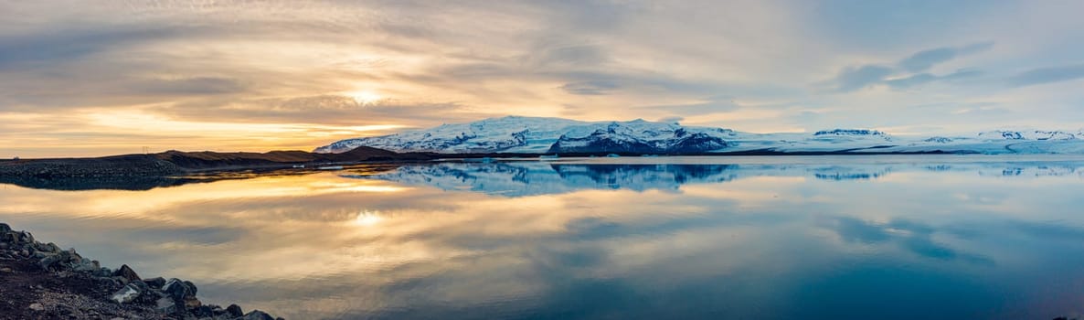 Icelandic panorama of frozen icy lake near snowy mountain tops, panoramic view of scandinavian landscape scenic route. Freezing arctic open water forming famous iceland scenery.