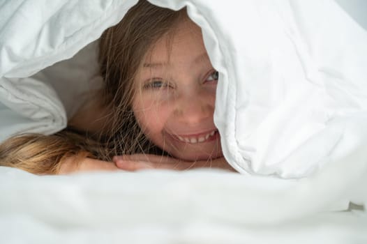 Portrait of a cute little girl laughing and hiding under the blanket