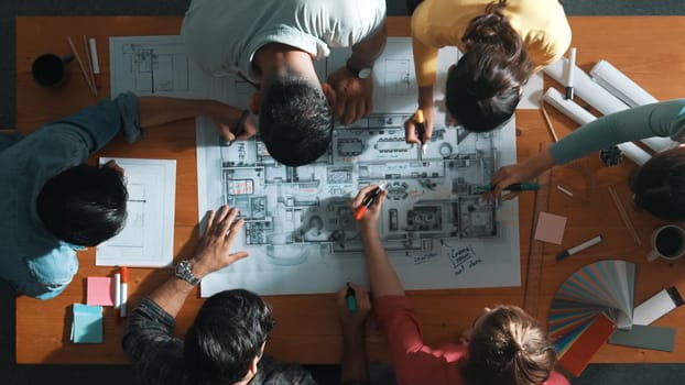 Top down view of civil engineer team writing at blueprint at meeting table with color palettes. Group of diverse people planning and taking a note while manager looking at project plans. Symposium.