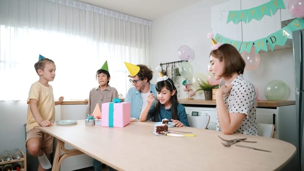 Caucasian mom cutting birthday cake and separated dessert while give to father. Happy family wear party hat to celebrated daughter birthday while sitting at table. Special occasion concept. Pedagogy.