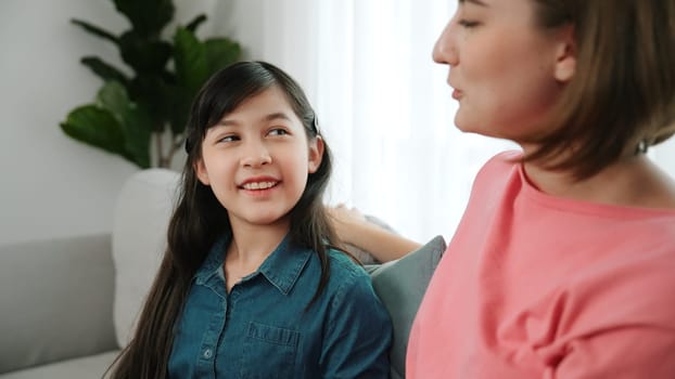 Happy mother sharing experience with daughter while sitting in living room. Caucasian mom and happy child talking and spend time together. Attractive girl listen parent story while smiling. Pedagogy.