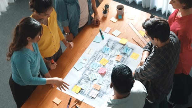 Top view of civil engineer team writing at blueprint at meeting table with color palettes. Group of smart diverse people planning and taking a note while manager looking at project plans. Symposium.