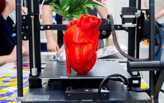 3D printer and model of human heart printed on 3D printer. Red prototype of human heart printed on 3D printer on a 3D printer desktop. New modern additive printing medical healthcare technologies