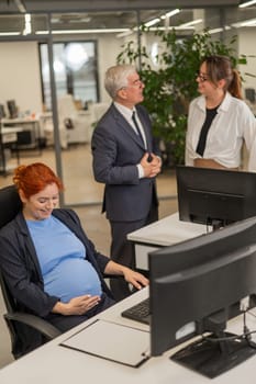 Happy Caucasian pregnant woman sitting at her desk, colleagues gossiping behind her back. Vertical photo