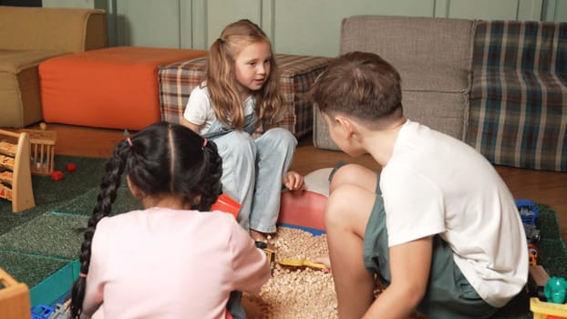 Diverse smart students play sandbox at play room. Multicultural children playing, digging and building sand castle with plastic toy while sitting at school in art lesson. Creative activity. Erudition.