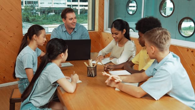 Caucasian teacher and smart boy discuss about project at classroom. Professional instructor talking about classwork while giving a paper to highschool child with diverse student listen. Edification.