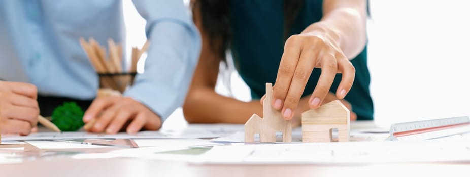 Professional architect engineer team discussion about architectural project on meeting table with wooden block and blueprint scatter around. Design and cooperate concept. Closeup. Delineation.