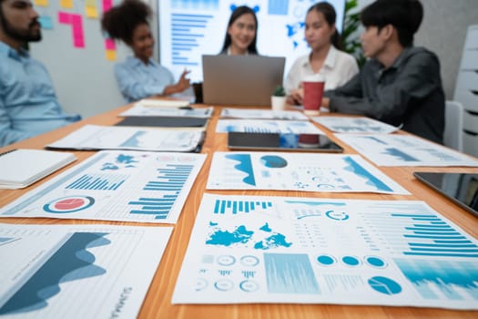 Focus financial dashboard paper showing graphs and chart with blurred background of diverse business people analyzing business data by BI Fintech technology for business marketing indication. Concord