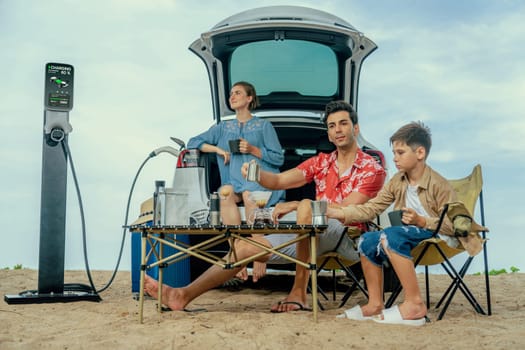 Family vacation trip traveling by the beach with electric car, happy family recharge EV car, enjoying outdoor camping coffee. Seascape travel and eco-friendly car for clean environment. Perpetual