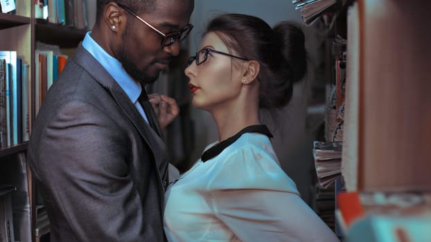 A black man and a white sexy girl stand face to face in the library. The temptation and passion between students of interracial affiliation.Yaremche, Bukovel, Ukraine - January 10, 2022