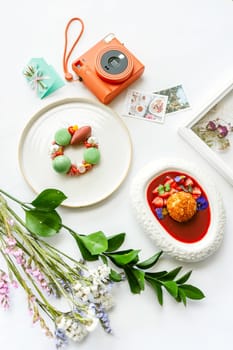 Beautiful background with two desserts, polaroid camera and flowers. Top view on white table