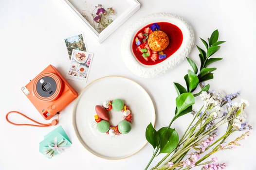 Beautiful background with two desserts, polaroid camera and flowers. Top view on white table