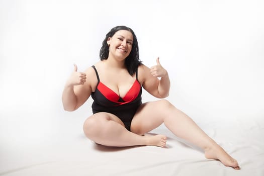 Portrait of attractive dreamy thick woman in red black swimsuit posing on white background. Body positive, photoshoot, selfie. Funny plus size model