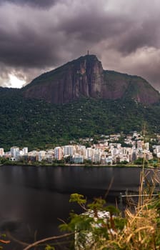 Dramatic clouds and a statue atop a mountain overlook a bustling cityscape.