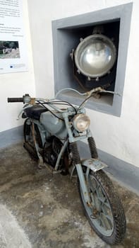 Asinara, Italy. August 11, 2021. Ancient motorcycle and a large headlight at the entrance to the prison museum on the hill of the island.
