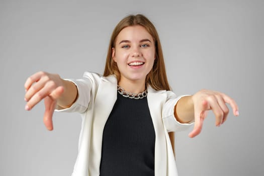 Young Woman in White Blazer Pointing at You Against a Grey Background in Studio