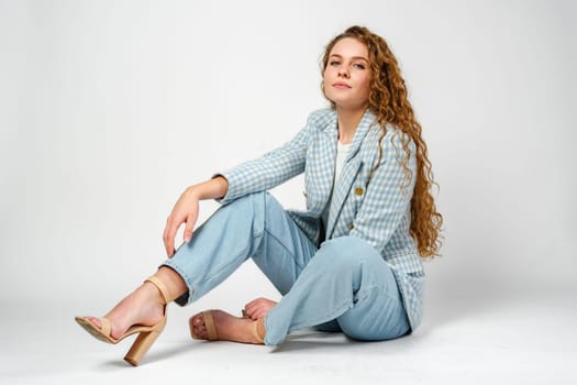 Young woman with curly hair in blue jacket posing on gray background close up