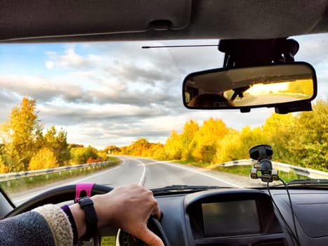 Car salon, windshield, hand of woman on steering wheel and landscape. View from seat of female driver on nature and Road, trees, blue sky at sunny day