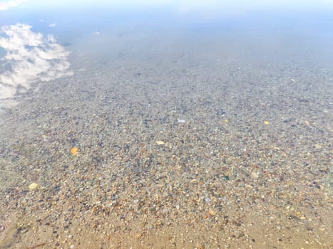 Pebbles in the water. Background, texture. Shallow Riverbed With Colorful Pebbles at Daytime. Clear water flowing over a multicolored pebble bed