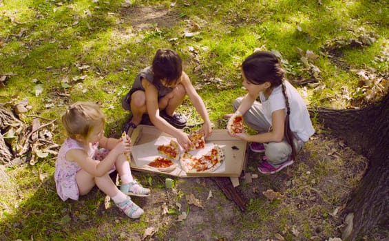 Breakfast on the grass. Three girls sitting in the park and eating pizza.