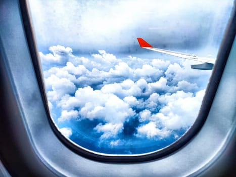 Clouds and a wing through a porthole in an airplane. Aerial View of Fluffy Clouds and Airplane Wing From Cabin Window. Wing above vibrant cloud