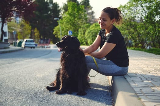 Happy young woman enjoying the outdoors with her pet dog. Pretty female walking her black cocker spaniel on leash. The concept of love, care and empathy for domestic animals. Playing pets