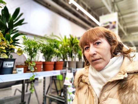 Middle-Aged girl in a flower and plant shop. Mature Woman Shopping for Seedlings at Plant Nursery in Spring
