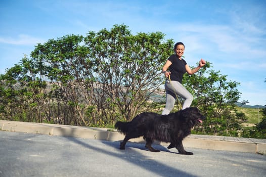 Full length portrait of a mixed race young active woman running and walking her dog on leash on the nature outdoors. People. Playing pets. Sport. Active and healthy lifestyle concept