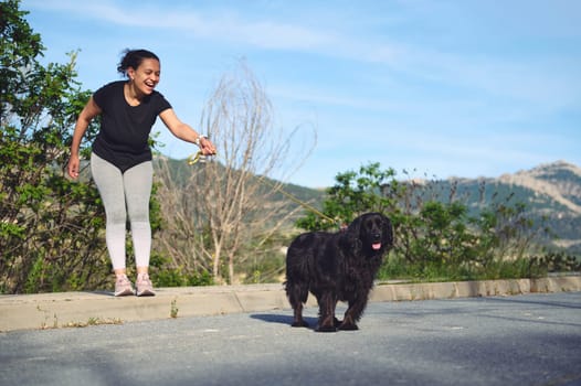 Happy cheerful woman enjoying a walk with her dog on leash in the nature. A black cocker spaniel pet being walked in the mountains nature