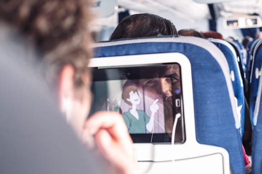 Reflection of a passenger on an airplane touch screen monitor while watching cartoon during long flight. Entertainment service system in aircraft