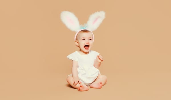 Portrait of cute baby with easter rabbit ears sitting on brown studio background