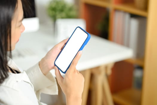 Close up young woman holding smartphone with blank screen sitting at her workplace.