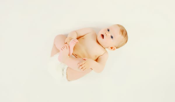 Cute baby in diapers lying on the floor on white studio background