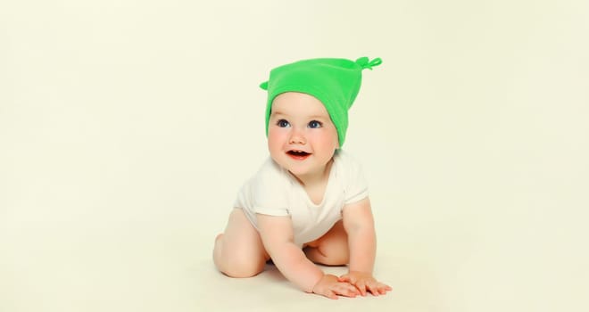 Happy cheerful baby in green hat playing on the floor on white studio background