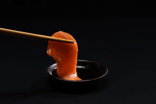 Closeup chopsticks with fresh salmon sashimi dipping into soy sauce. Japanese food style.