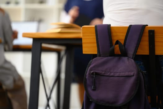 School backpack hanging on a wooden chair in classroom. Back to school concept.