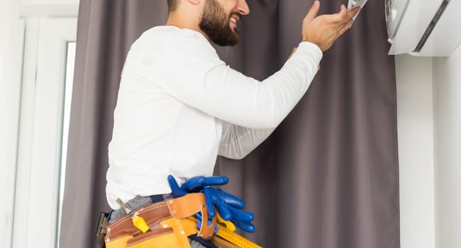 Male technician repairing air conditioner indoors.