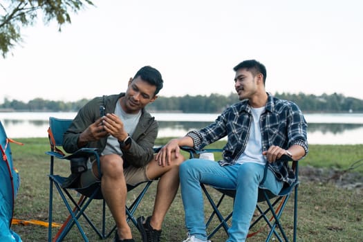 Gay LGBTQIA couple sitting on picnic chair drinking tea and coffee while camping on vacation holiday.