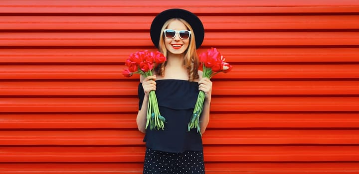 Portrait of beautiful happy smiling woman with bouquet of red rose flowers in black round hat