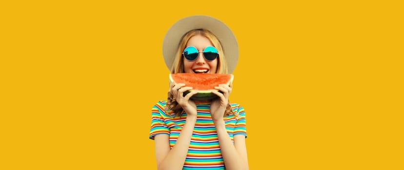 Summer portrait of happy young woman eating fresh slice of watermelon in straw tourist hat, sunglasses on colorful yellow studio background