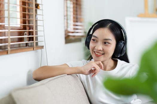 Happy asian woman listening to music from mobile phone while sitting on the the sofa at home.