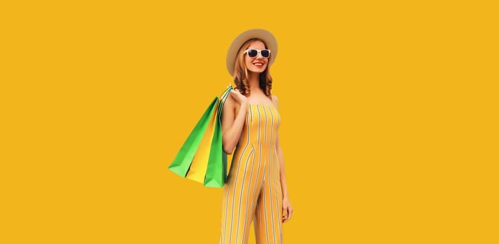 Stylish beautiful happy young woman model with shopping bags in summer straw hat on yellow studio background