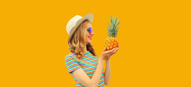 Summer portrait of happy smiling young woman with pineapple fruit in straw tourist hat, sunglasses on yellow studio background