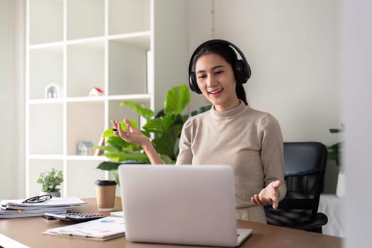 Young businesswoman wearing headphones and discussing project detail with clients on video call. woman with headphones conducting online meeting with colleagues.