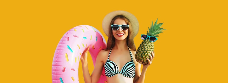 Summer vacation, tourism, happy smiling young woman with swimming inflatable ring and pineapple wearing straw hat on yellow studio background