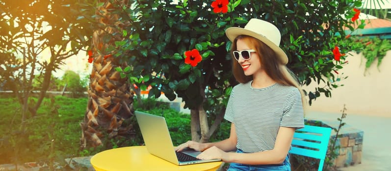 Happy young woman working with laptop sitting at the table in street cafe in summer park