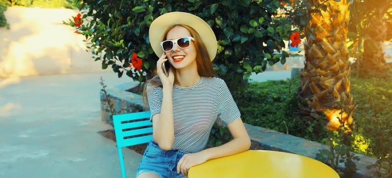 Happy modern smiling young woman calling on mobile phone sitting on the table waiting in street cafe in summer park