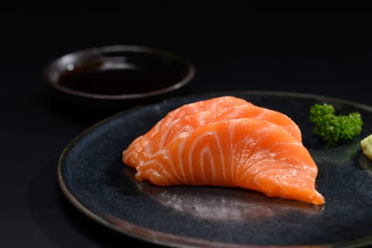 Close up sliced salmon sashimi serve on black plate with parsley leaf. Japanese food style.