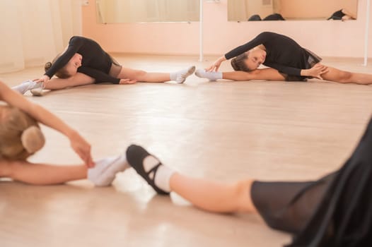 Little girls sit in a circle and do stretching at a ballet school