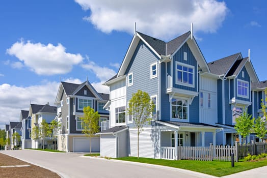 A perfect neighborhood. Brand new townhouses district on blue sky and clouds background.